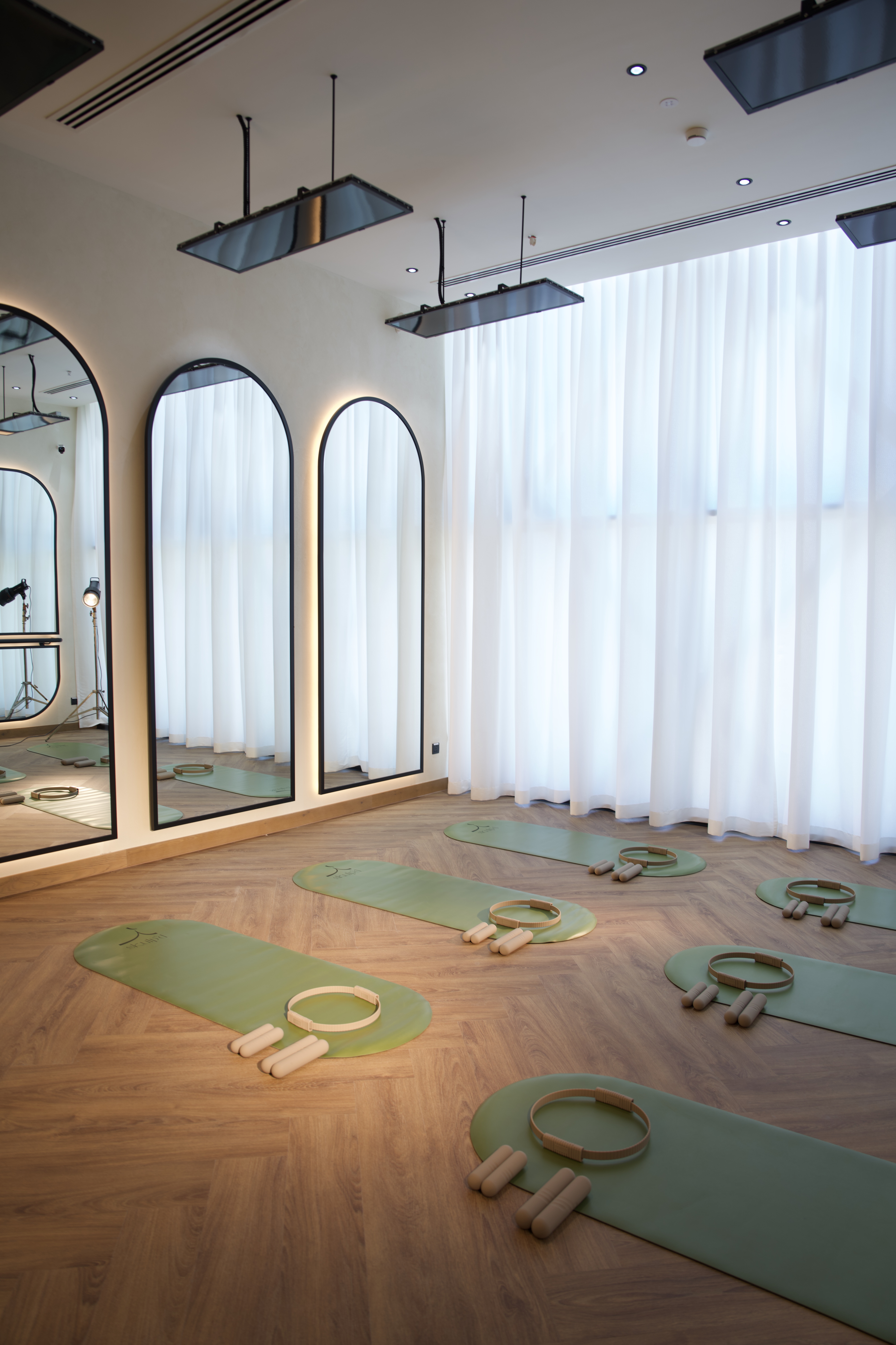 Infrared heating panels mounted above the Pilates studio floor at SKULP'D Dubai, with arched mirrors and sage green mats